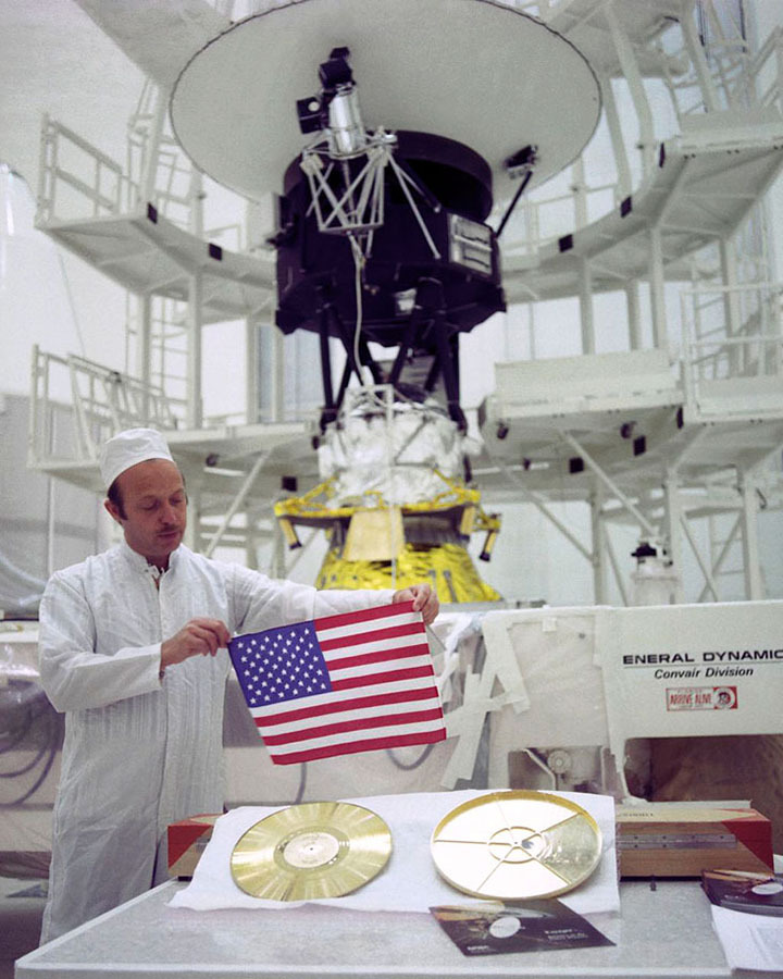 technician holding u.s. flag with voyager spacecraft in background