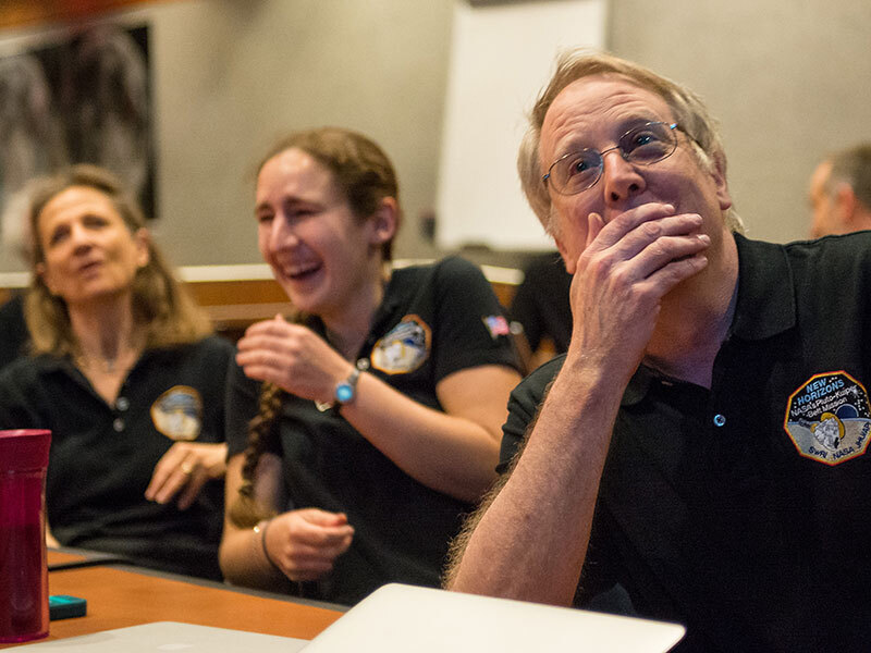 Two women and a man smiling at photos coming down from Pluto in 2015,