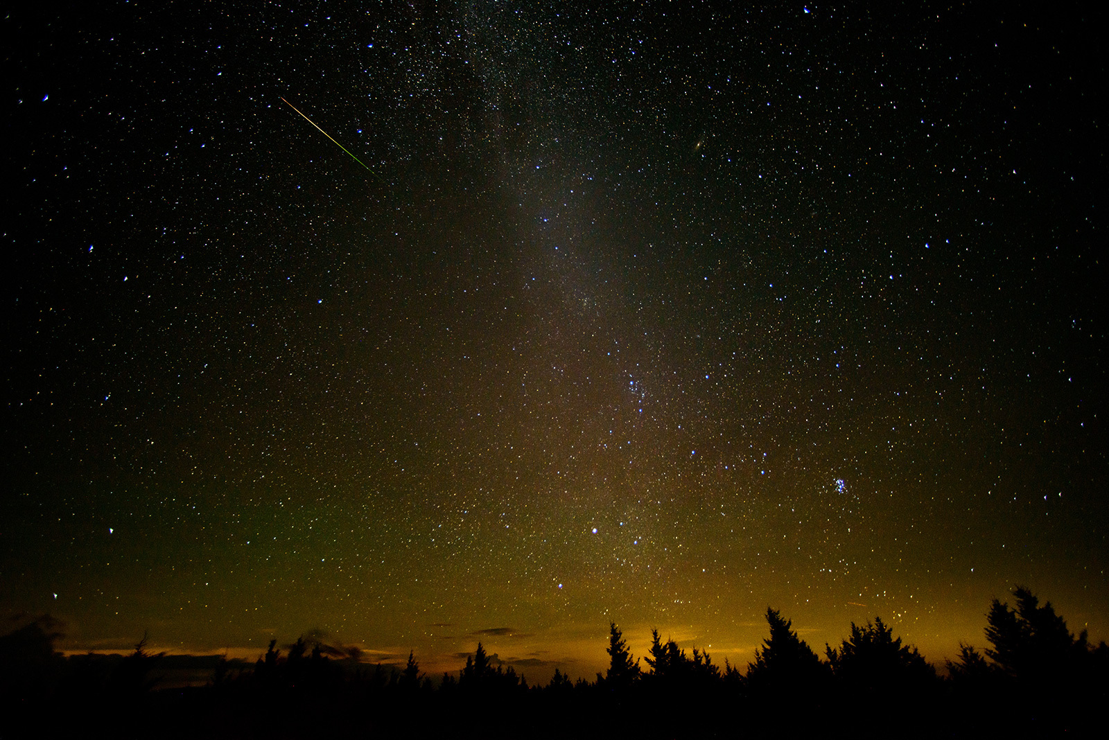 Meteor over a forest with twilight on the horizon.