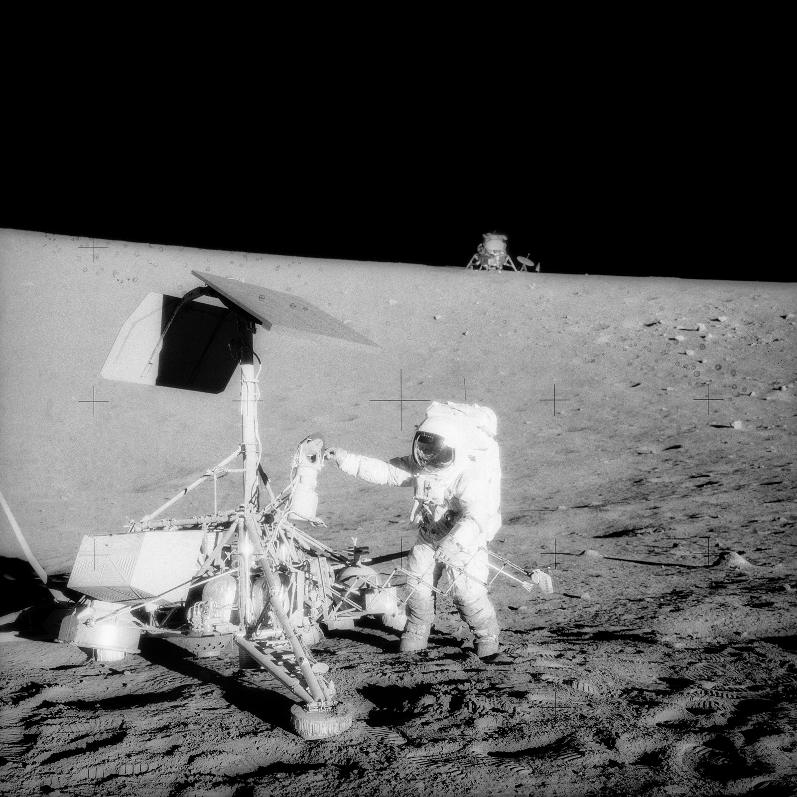 Astronaut standing next to robotic spacecraft on the surface of the Moon.