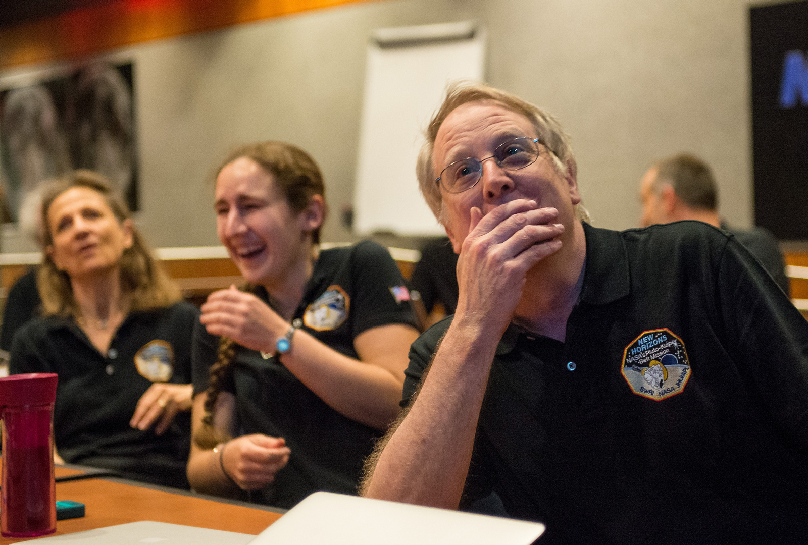 Two women and a man react with joy at seeing the first images of Pluto.