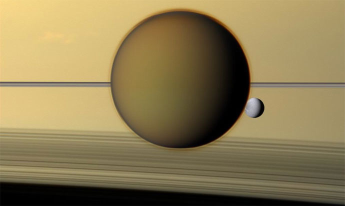 Dione can be seen through the Titan haze in this view of the two posing before the planet and its rings from Cassini.