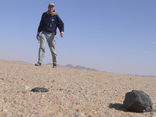 Man standing over meteorite in desert.
