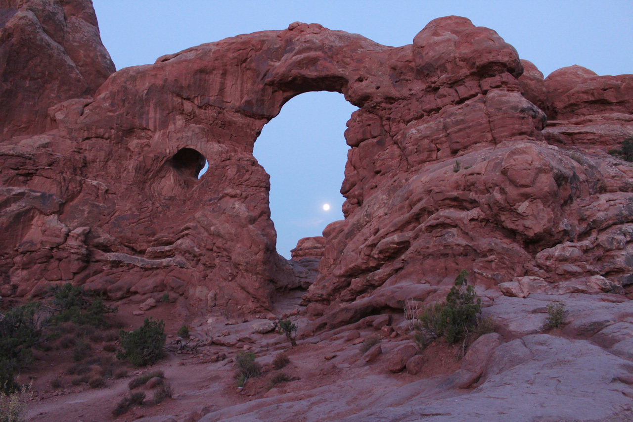Moon viewed between the arch of a desert rock formation.