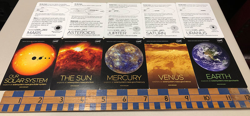 A partial set of trading cards set out along a 12-inch ruler for scale.