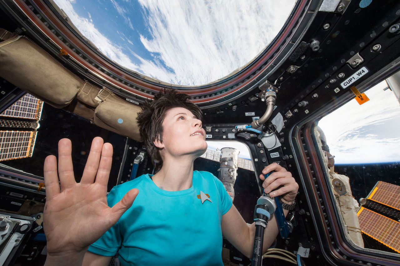 Woman astronaut displays the Vulcan salute -- spreading four fingers into a big "V" -- while looking down onto the Earth from space.