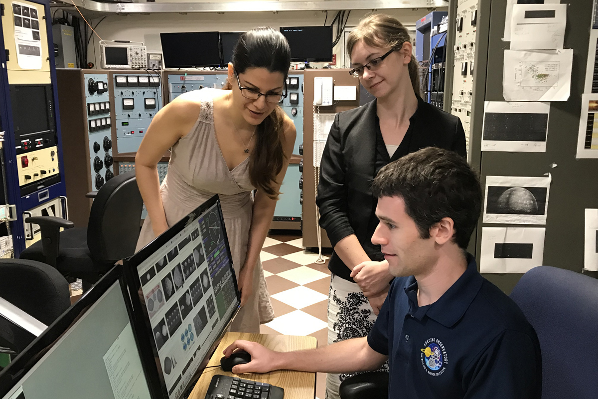 Two women and a man in a control room looking at asteroid images on a computer.