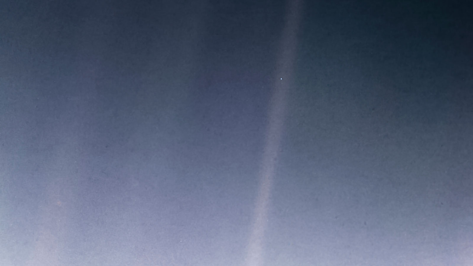 Distant view of Earth as a bright pale blue dot caught in a sunbeam.