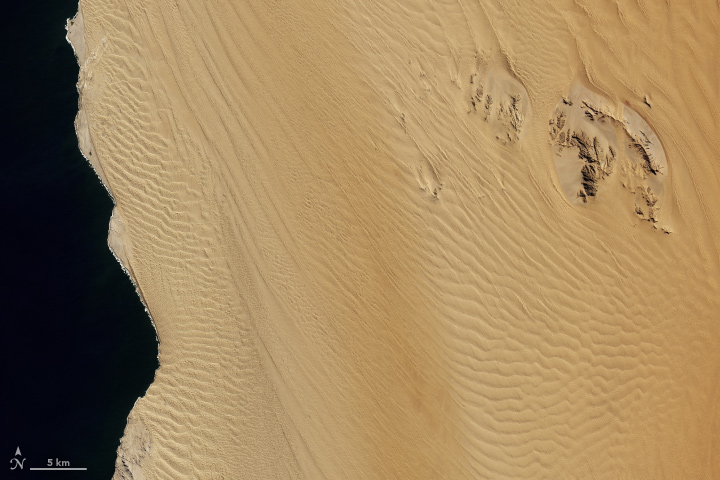 Satellite view of a rippling field of sand dunes, in true color. A 5 km scale bar spans the peaks of several ridges. 