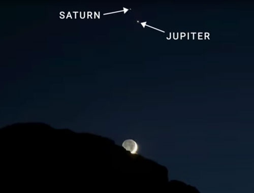 Jupiter and Saturn and the Moon behind a rocky peak.