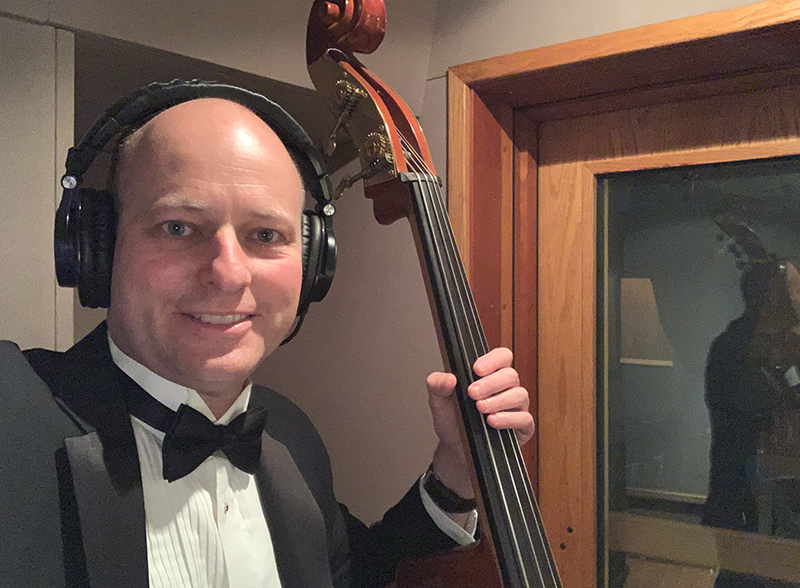 Jordan Evans wearing a tux, and holding a musical instrument inside a recording studio.