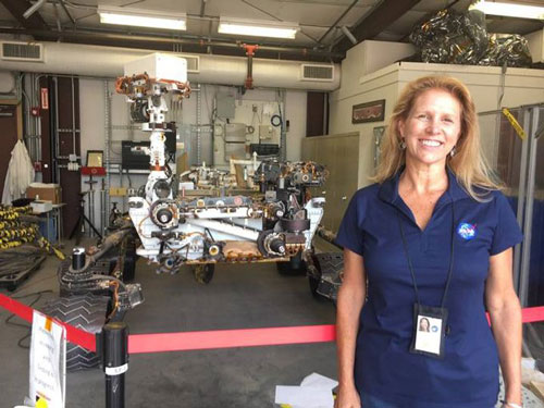 Photo of smiling Lori Glaze standing in front of the backup engineering model of the Mars Curiosity rover.