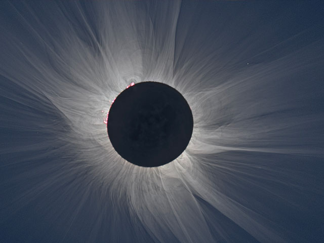 A total solar eclipse that shows white streams of light on a dark blue background coming of the Sun