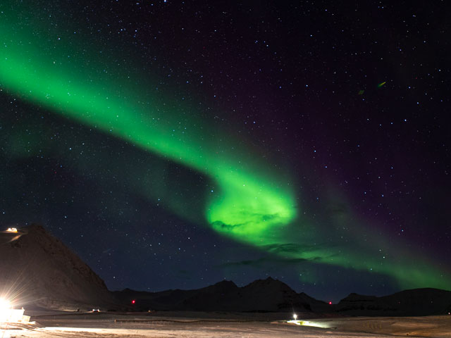 A green aurora over a starry night sky, about mountains and snow.