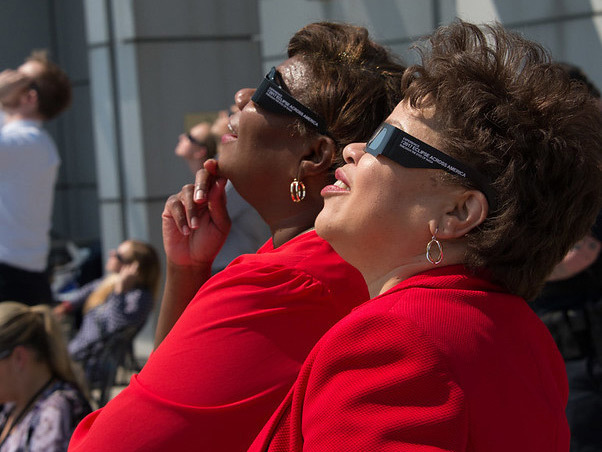 Two people look up at the Sun while wearing eclipse glasses