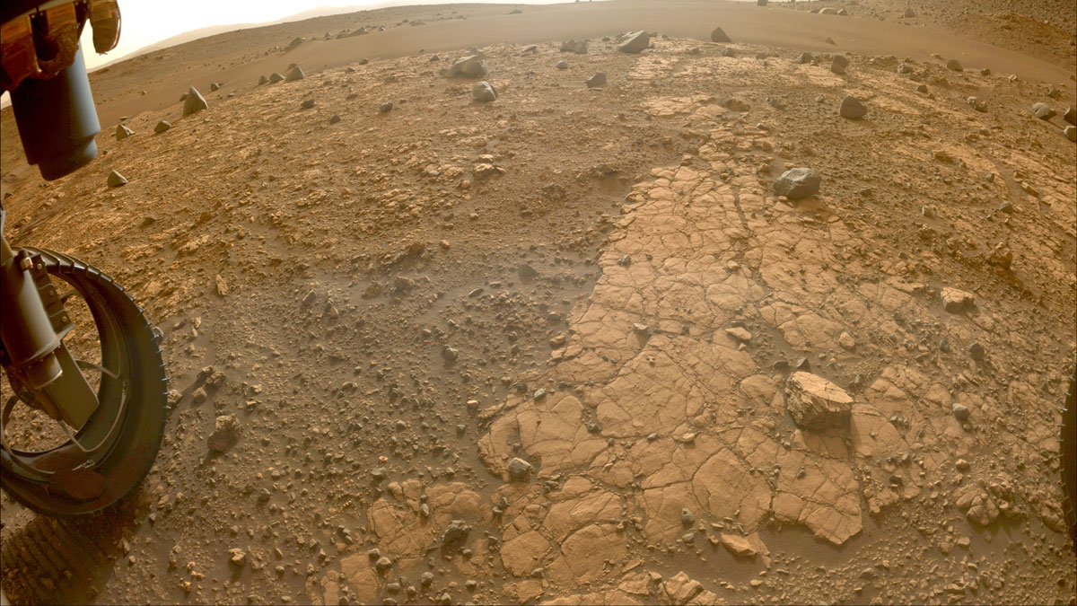A rover wheel is next to a rough, rocky slab of stone and soil.