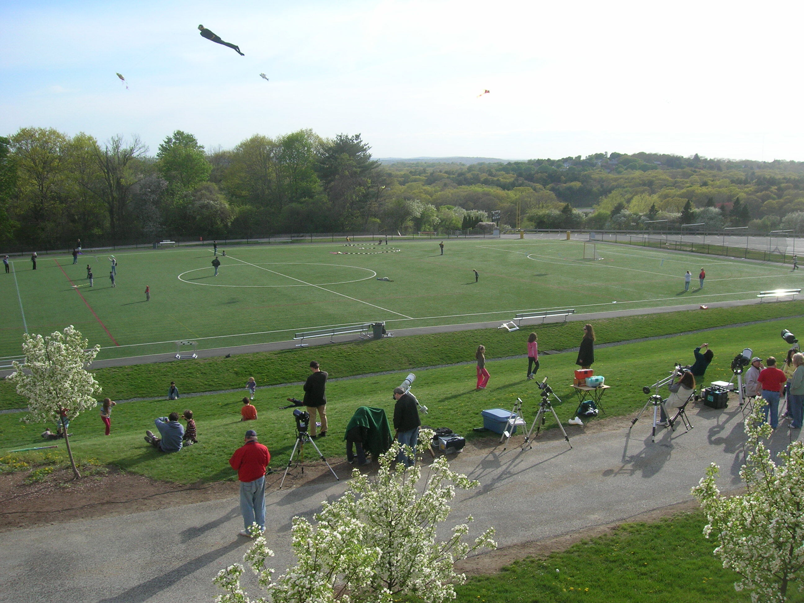 People stand scattered across a large soccer field flying kites.