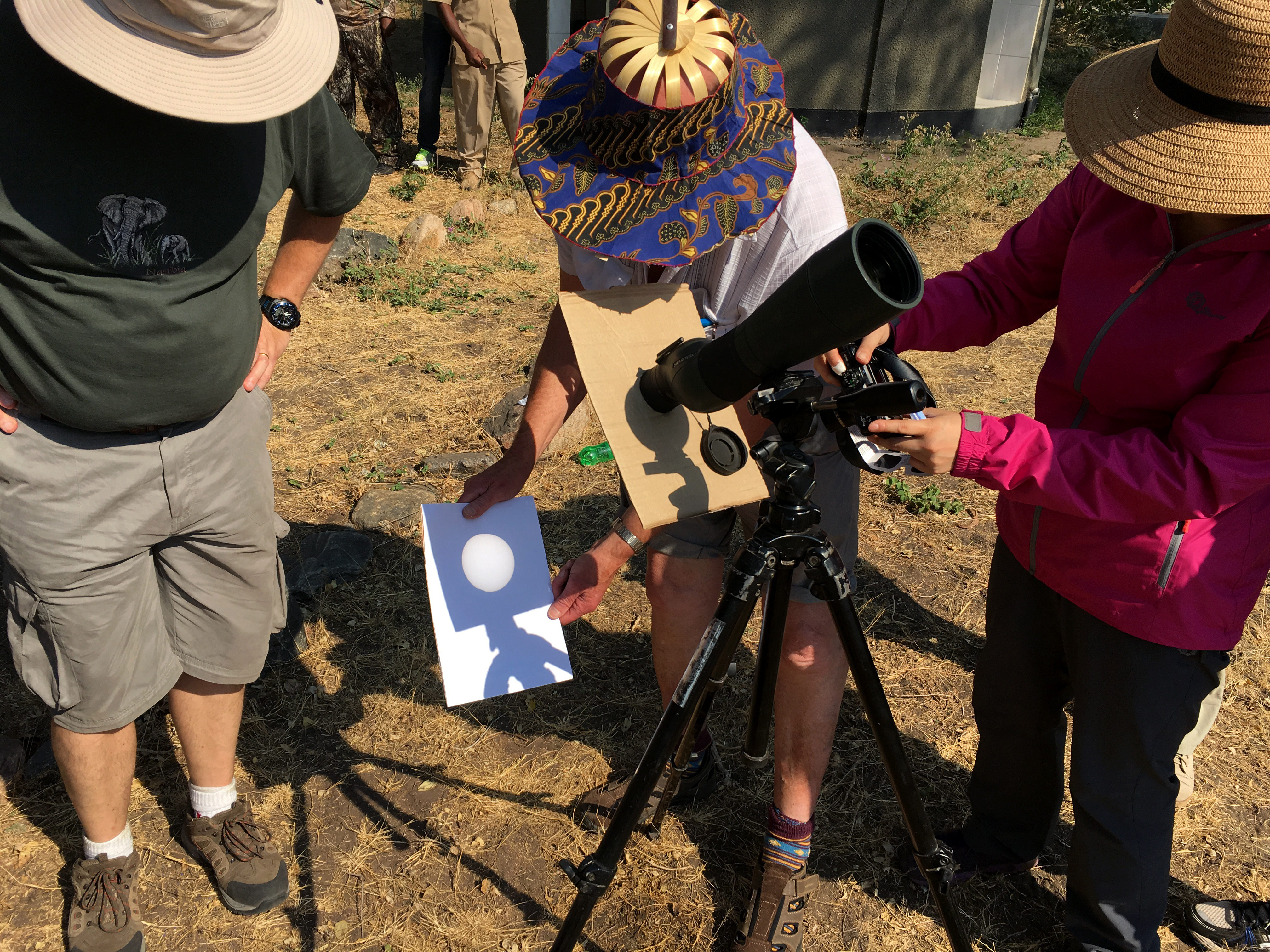 hree people stand around a telescope projecting an image of the Sun onto white paper