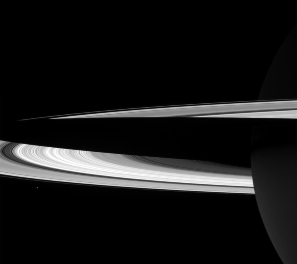 Shadow of Saturn falls across the rings in this black and white image. Tiny Janus hovers just below the rings.