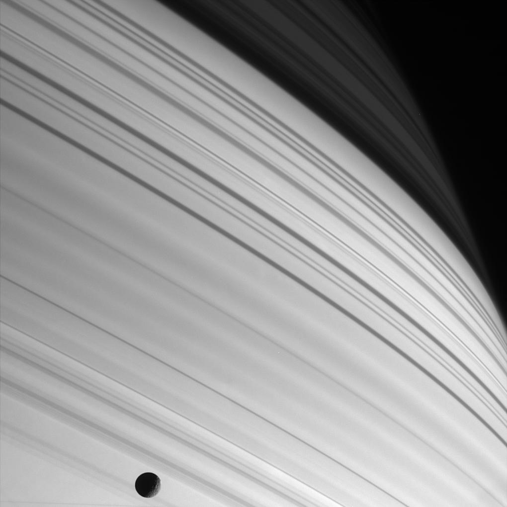Black and white image of sharp bands of sunlight with the moon mimas in the lower half of the image.