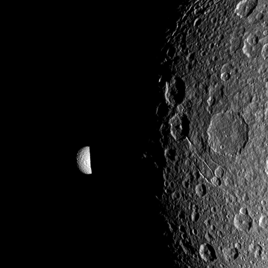 Mimas peeks out from behind the night side of Dione
