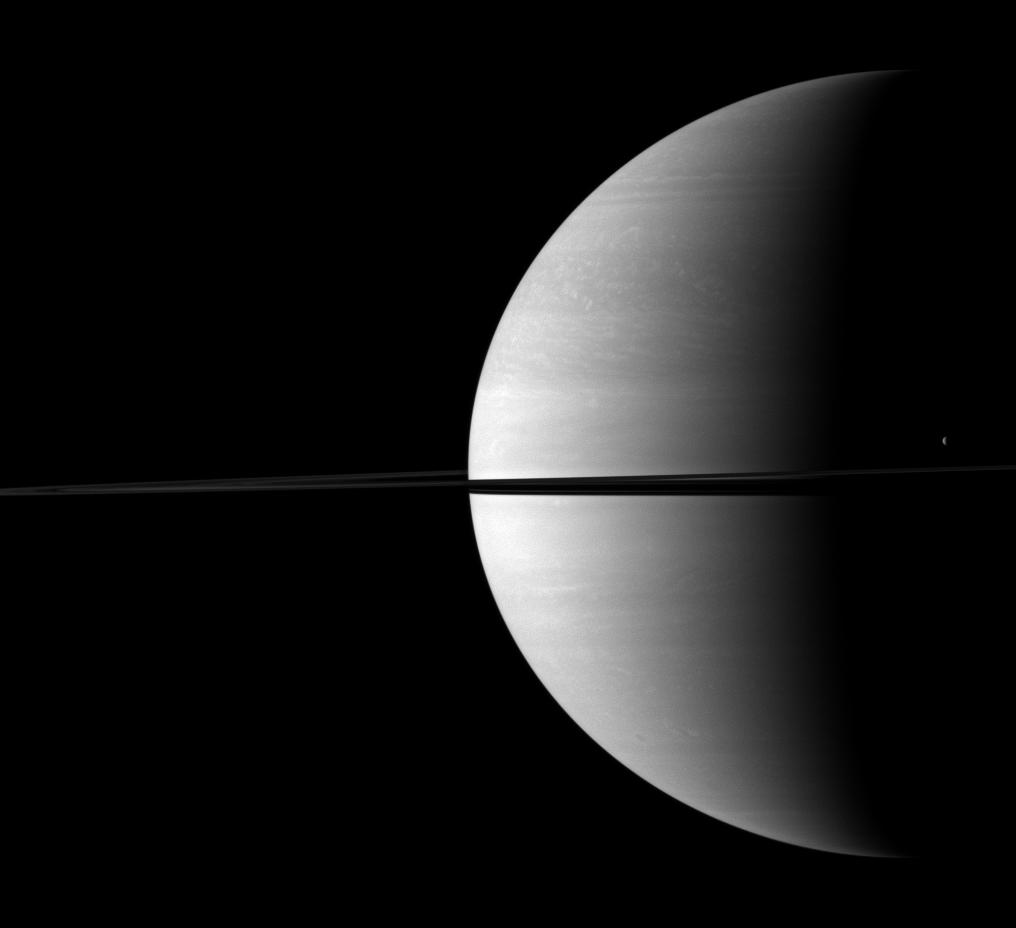 Tethys stands out as a tiny crescent of light in front of the dark of Saturn's night side