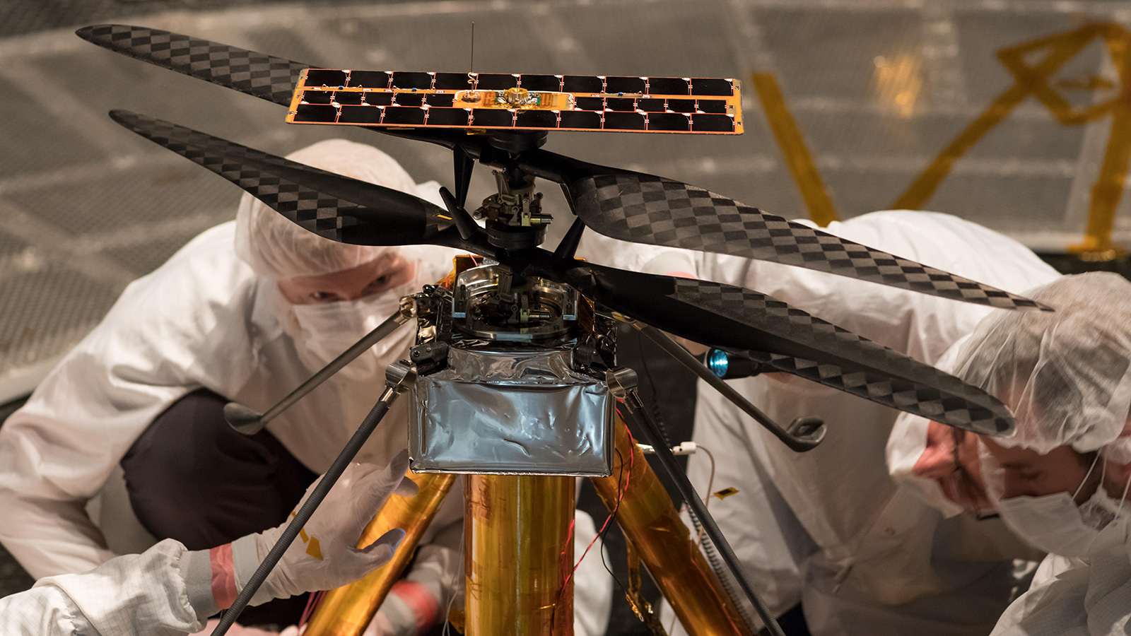 Engineers in clean suits inspect small helicopter.