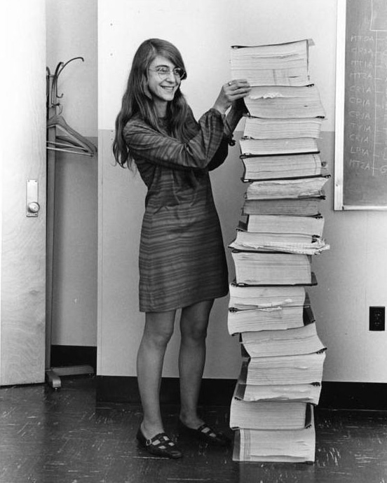 Smiling woman next to a huge printed stack of code that is as tall as she is.