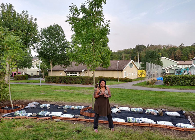 Rosa Castro rests a hammer on her shoulder in front of an unfinished gardening project in an open neighborhood.