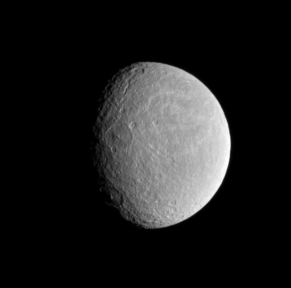 The sun's low angle near the terminator highlights the topography of craters within Rhea's wispy terrain.
