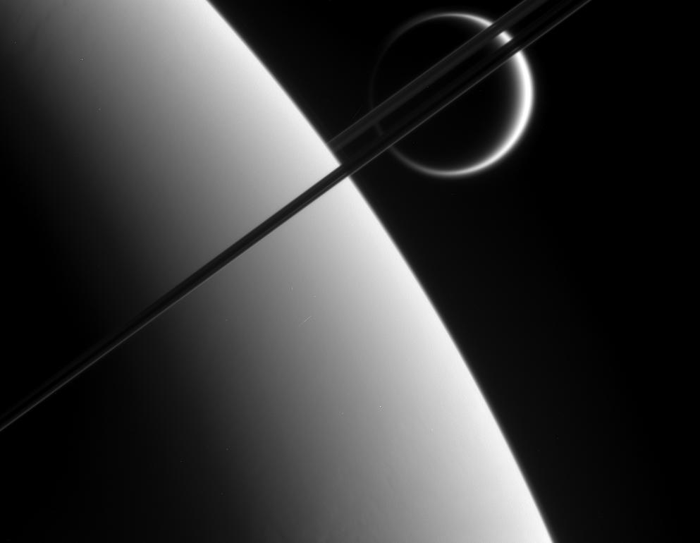 Titan in the distance beyond Saturn and its dark and graceful rings