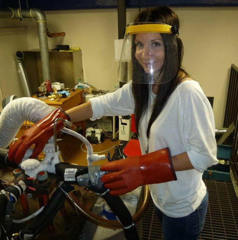 Adrienn Luspay-Kuti wearing orange gloves and a visor as she prepares to turn a white valve on a piece of equipment used in an experiment.