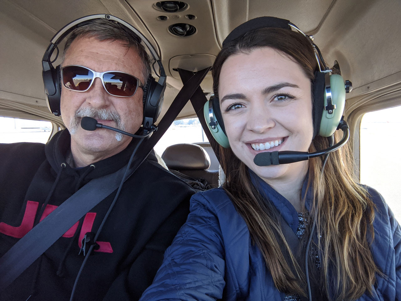 Smiling man and young woman in the cockpit of a small airplane.