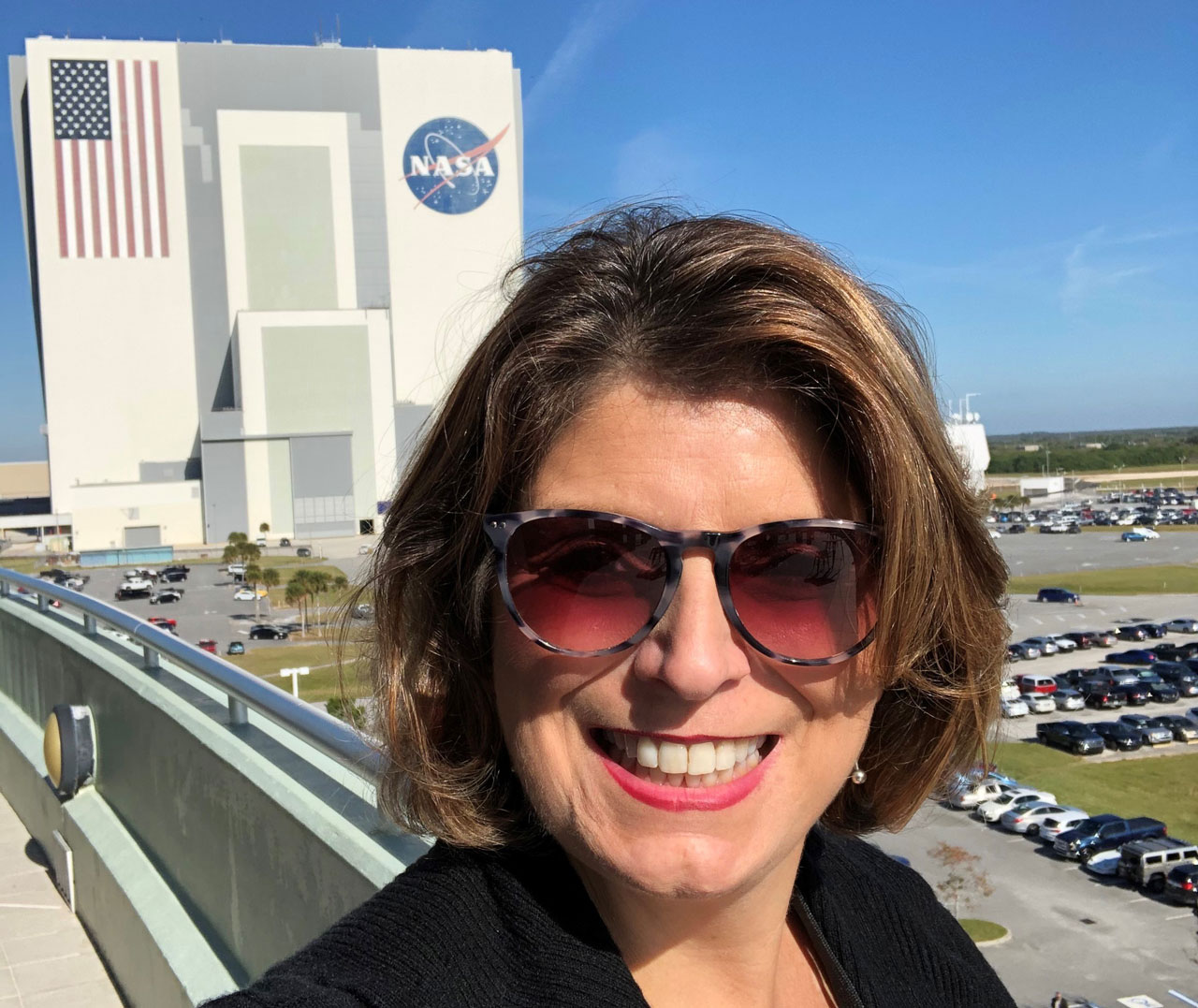 Photo of smiling woman in front of massive hanger at Kennedy Space Center in Florida.