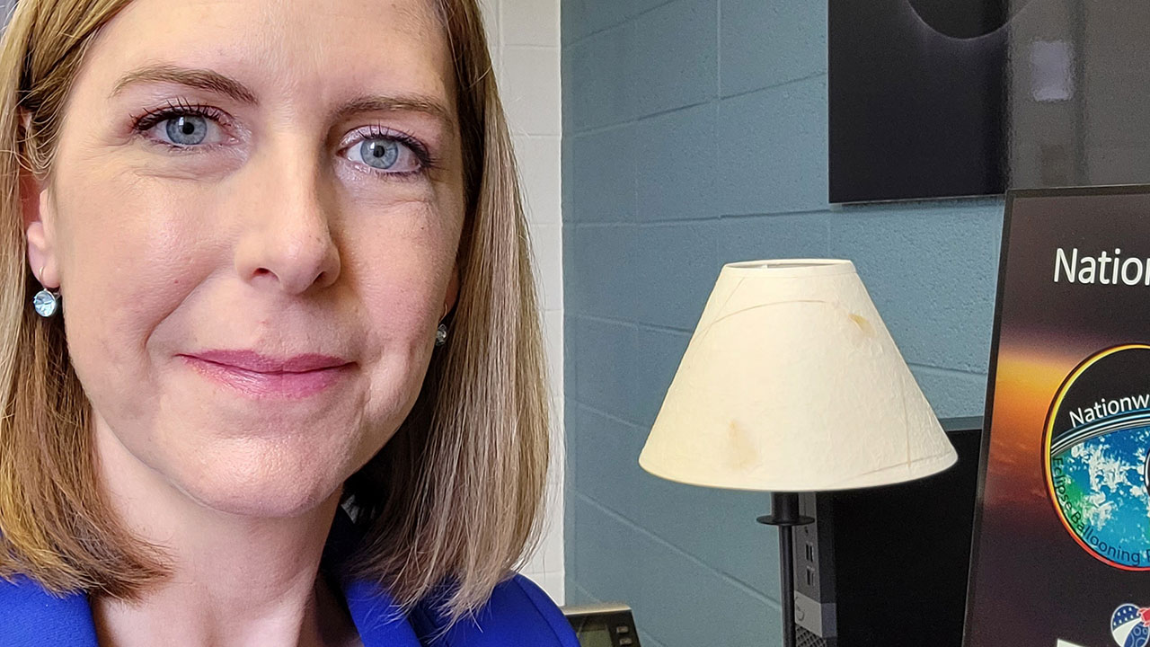 Angela is sitting in front of a computer wearing a purple jacket.