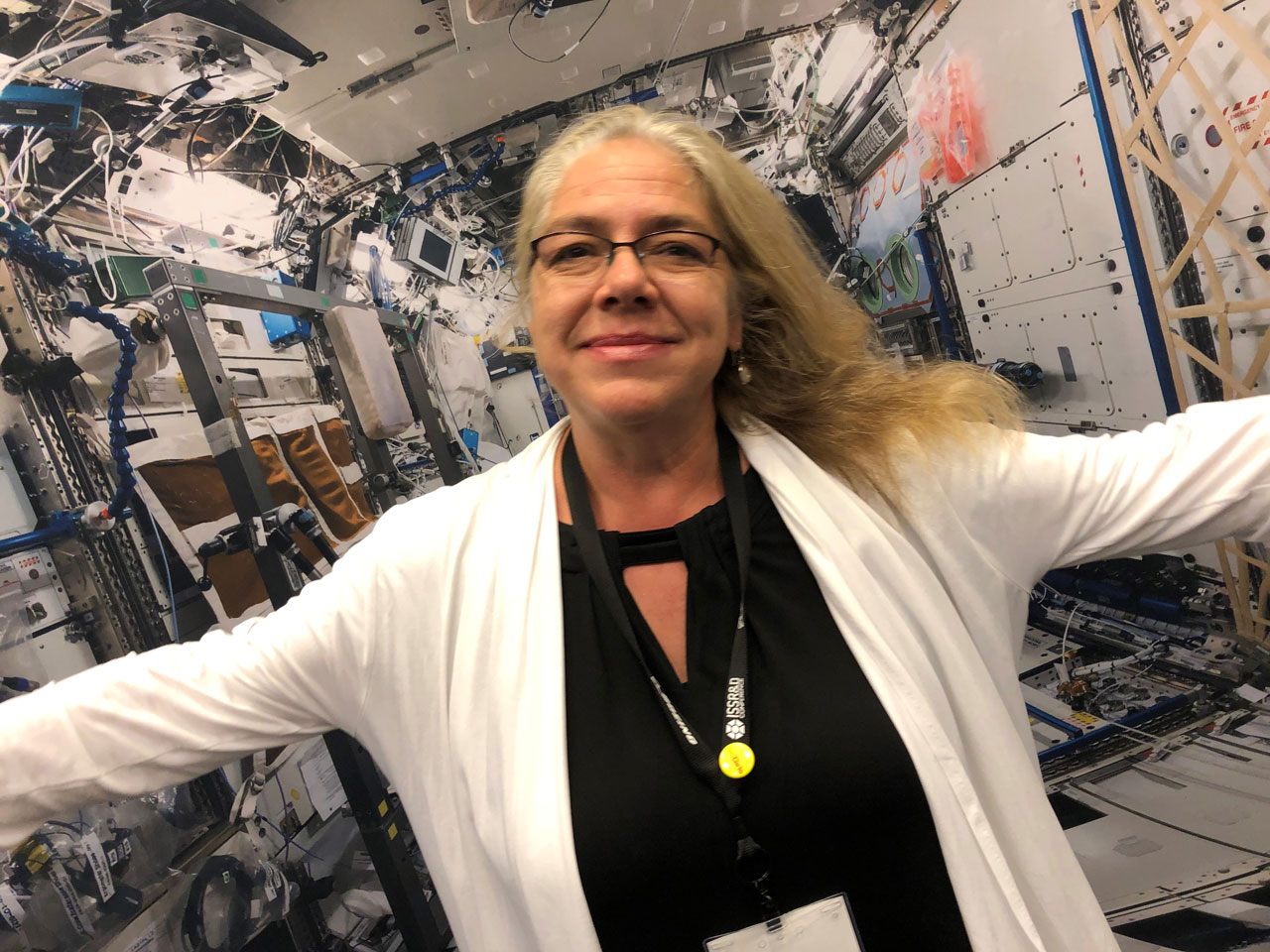 Rita in the space station simulator. The angle is tilted and her arms are spread wide so it looks as if she is floating in space.