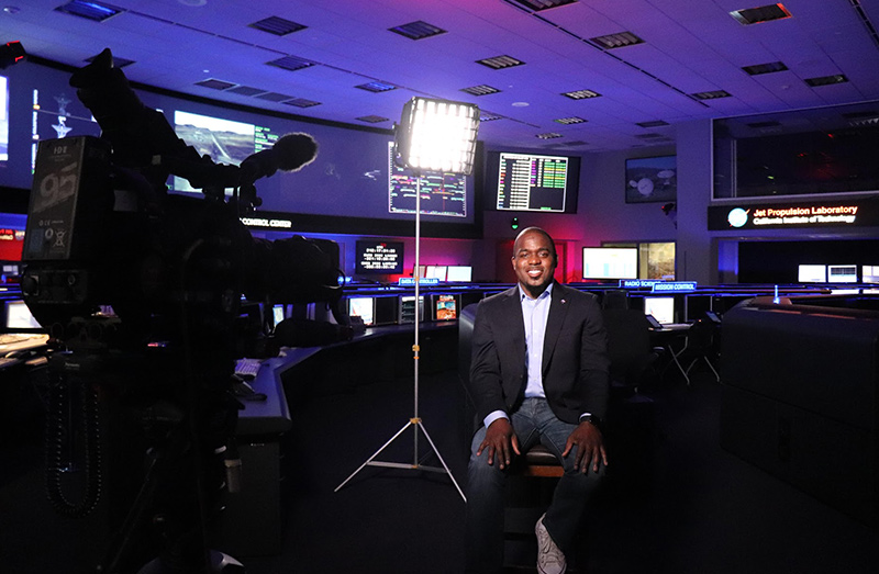 Dr. Alvin Smith sitting in a chair with a TV camera pointing at him and light shining on him.