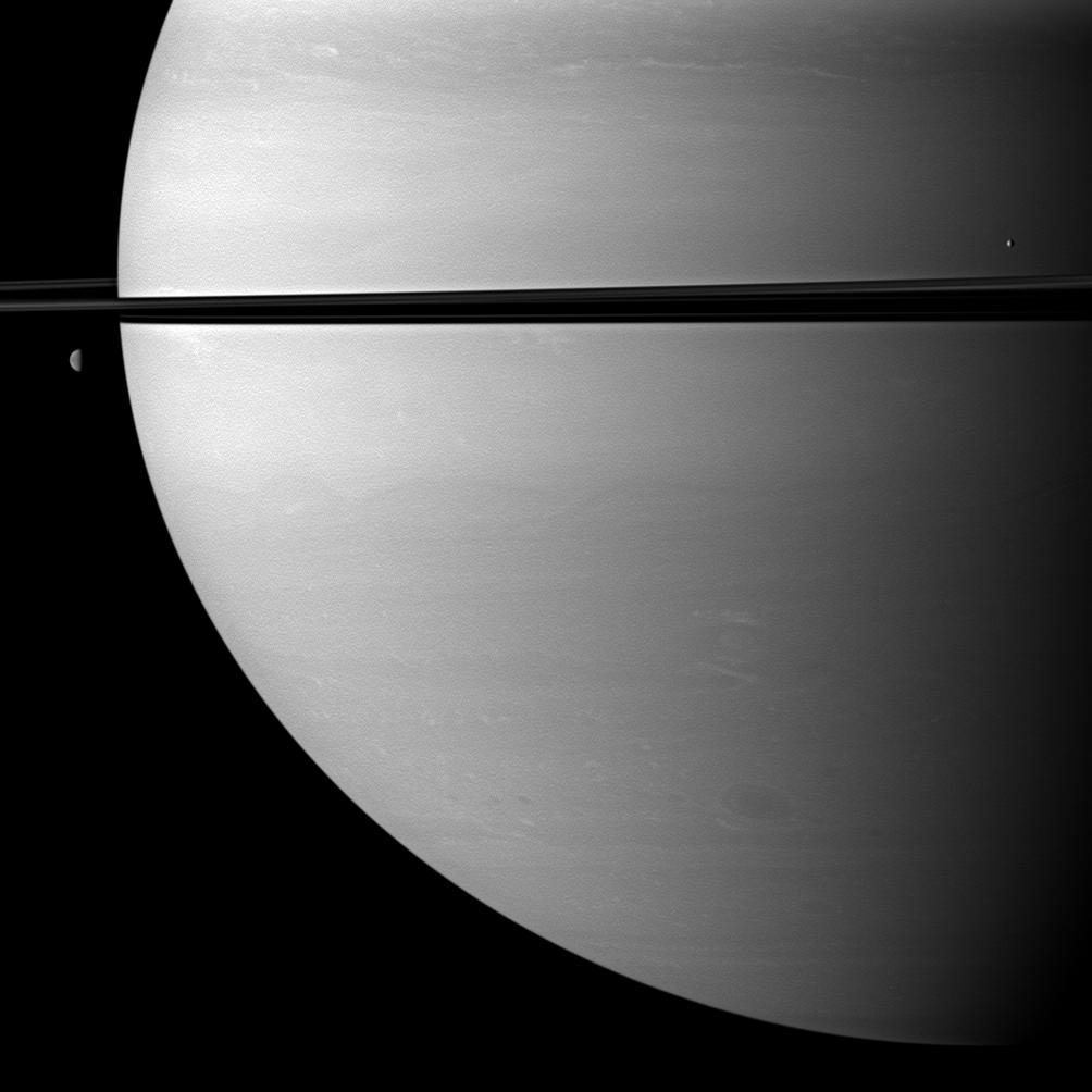 Two moons orbit serenely before Saturn while large storms churn through the planet's southern hemisphere.