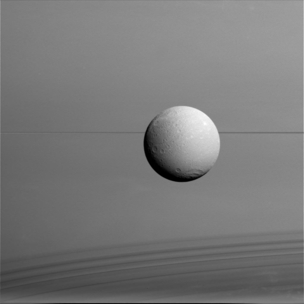 Dione hangs in front of Saturn and its icy rings in this view, captured during Cassini's final close flyby of the icy moon. 