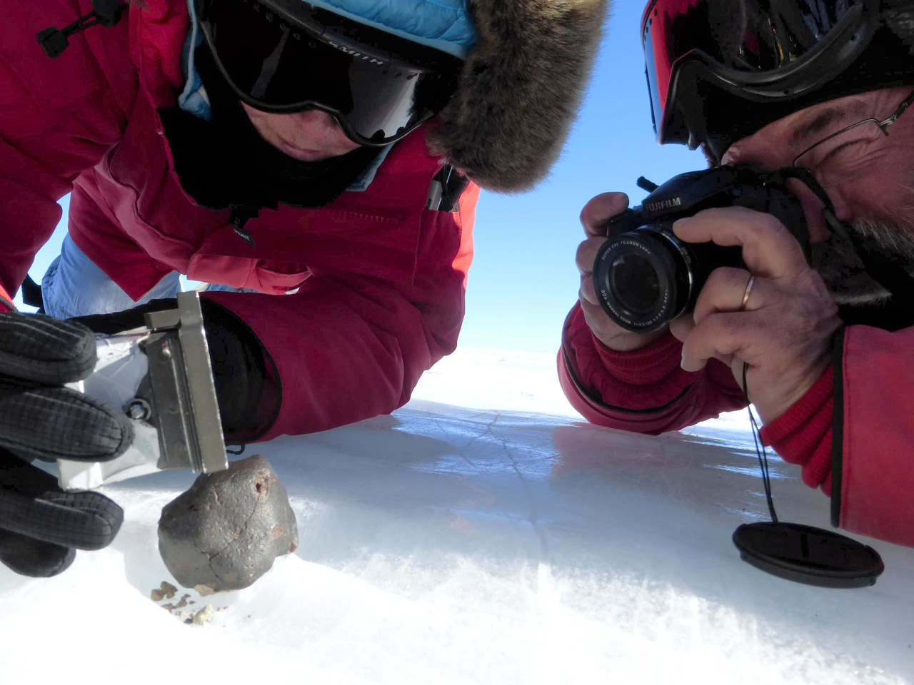 Two scientists examining a meteorite on snow-covered ground.