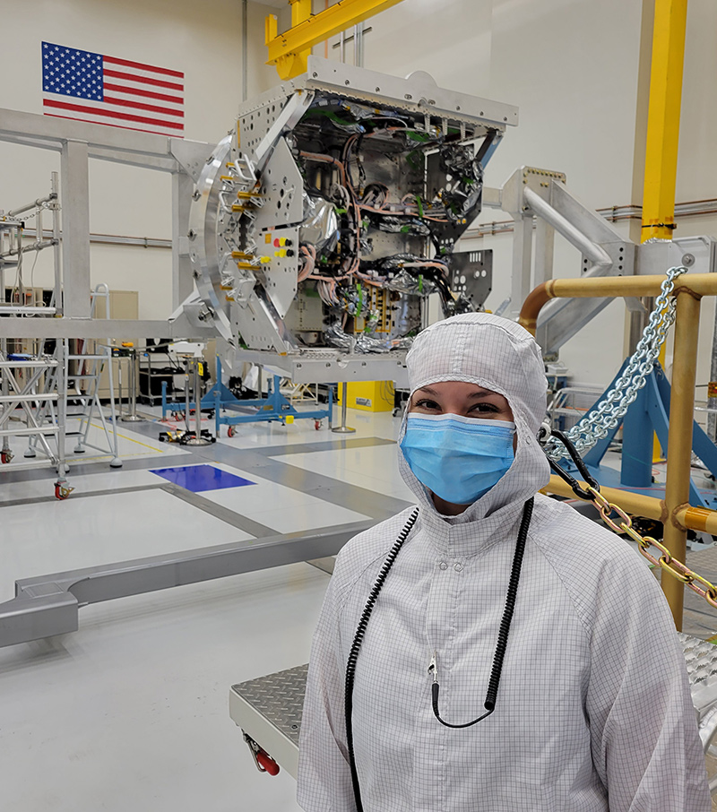 Valeria Salazar wears protective white clothing and a blue face mask as she stands near the Europa Clipper spacecraft, which is being assembled in a clean room at JPL.
