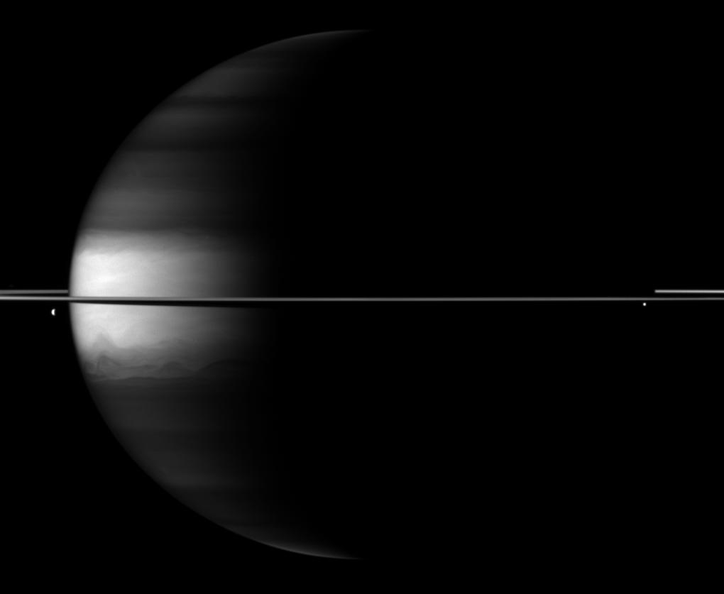 Dramatic differences between dark and light embellish this Cassini spacecraft image of Saturn, its rings and its moons Dione and Enceladus.