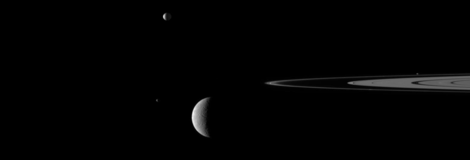 A gaggle of moons parade around Saturn's rings in this movie from Cassini in which the large moon Rhea passes in front of the small moon Janus.