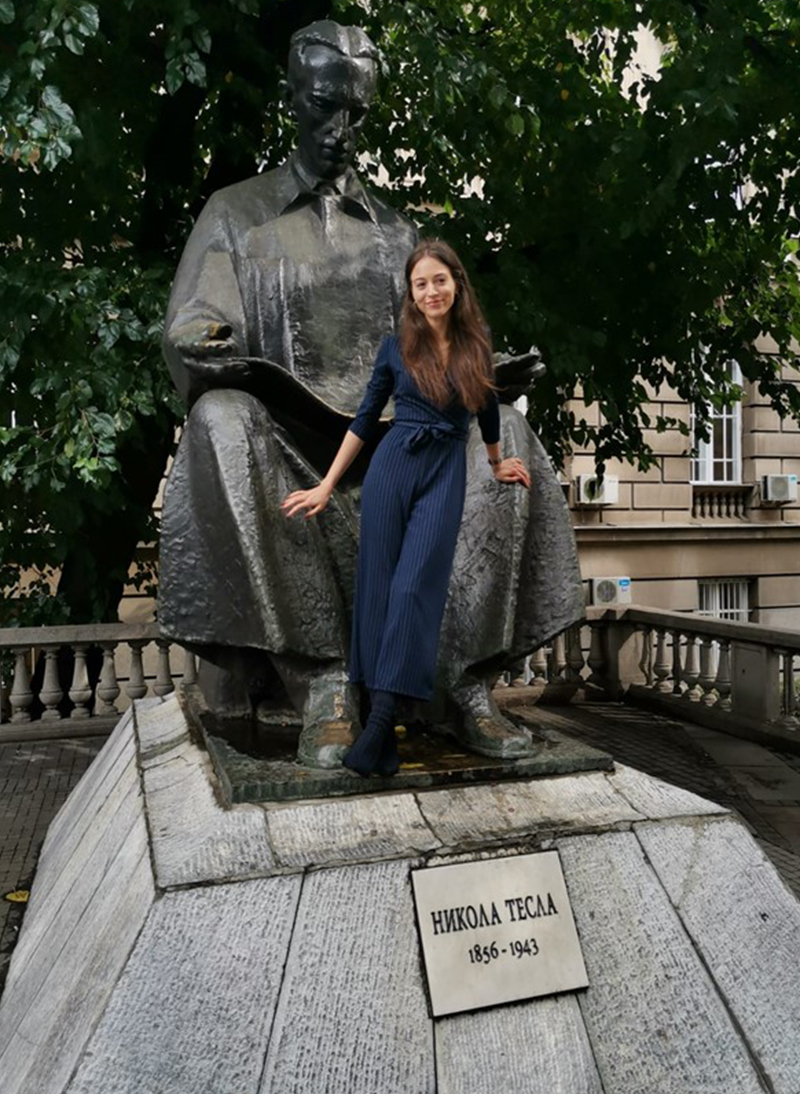 Tamara Stajić strikes a confident pose with a giant statue of Nikola Telsa.