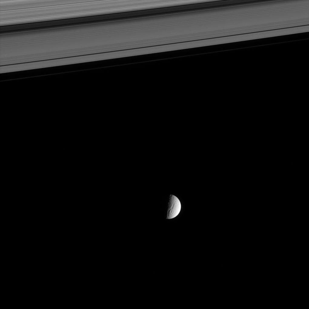 a distant view of Tethys beyond Saturn's rings