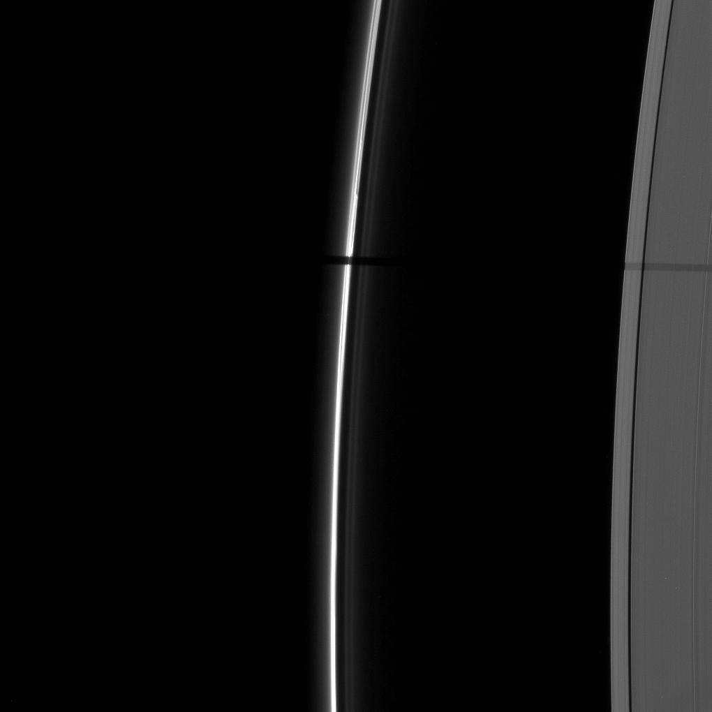 A wide shadow is cast onto the thin F ring and the A ring by the moon Janus