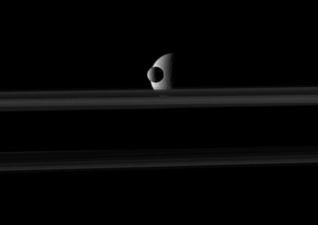 The small moon Mimas passes in front of the larger moon Rhea, which is partly obscured by Saturn's rings, in this movie from NASA's Cassini spacecraft.