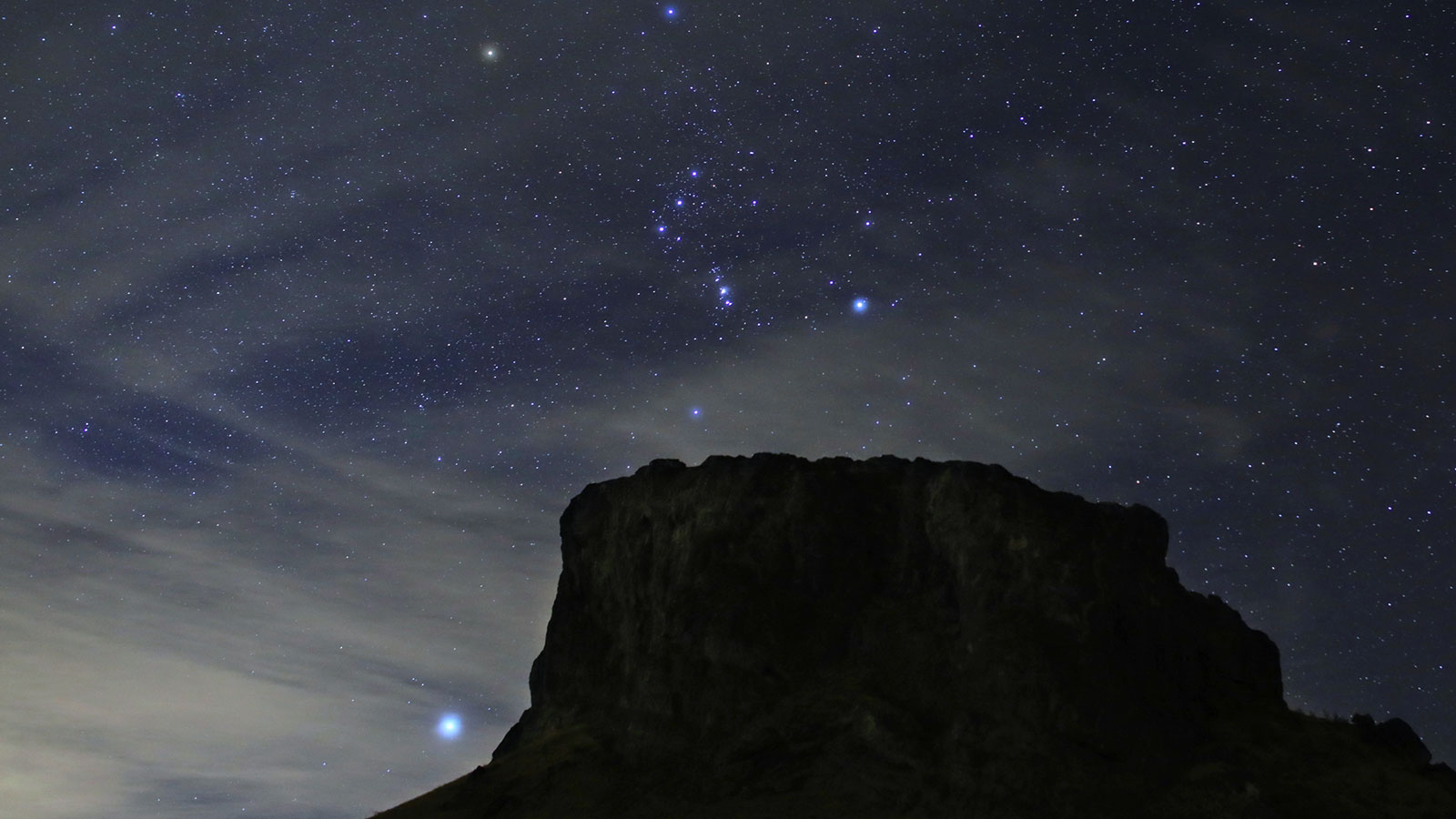 slide 1 - The bright contellation Orion rises above a flat top mesa in the southwestern desert.