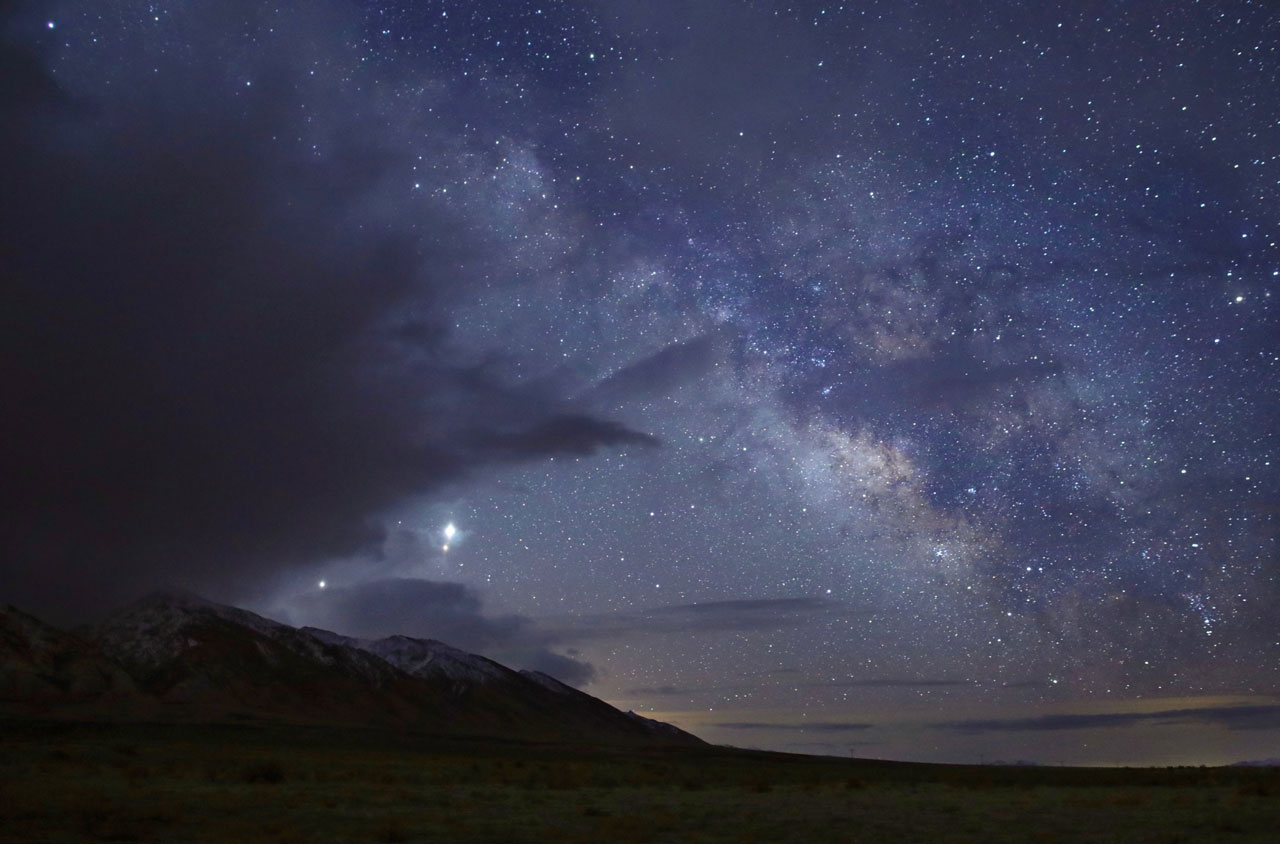 Three planets stand out among a twilight sky filled with stars over snow-capped mountains. 