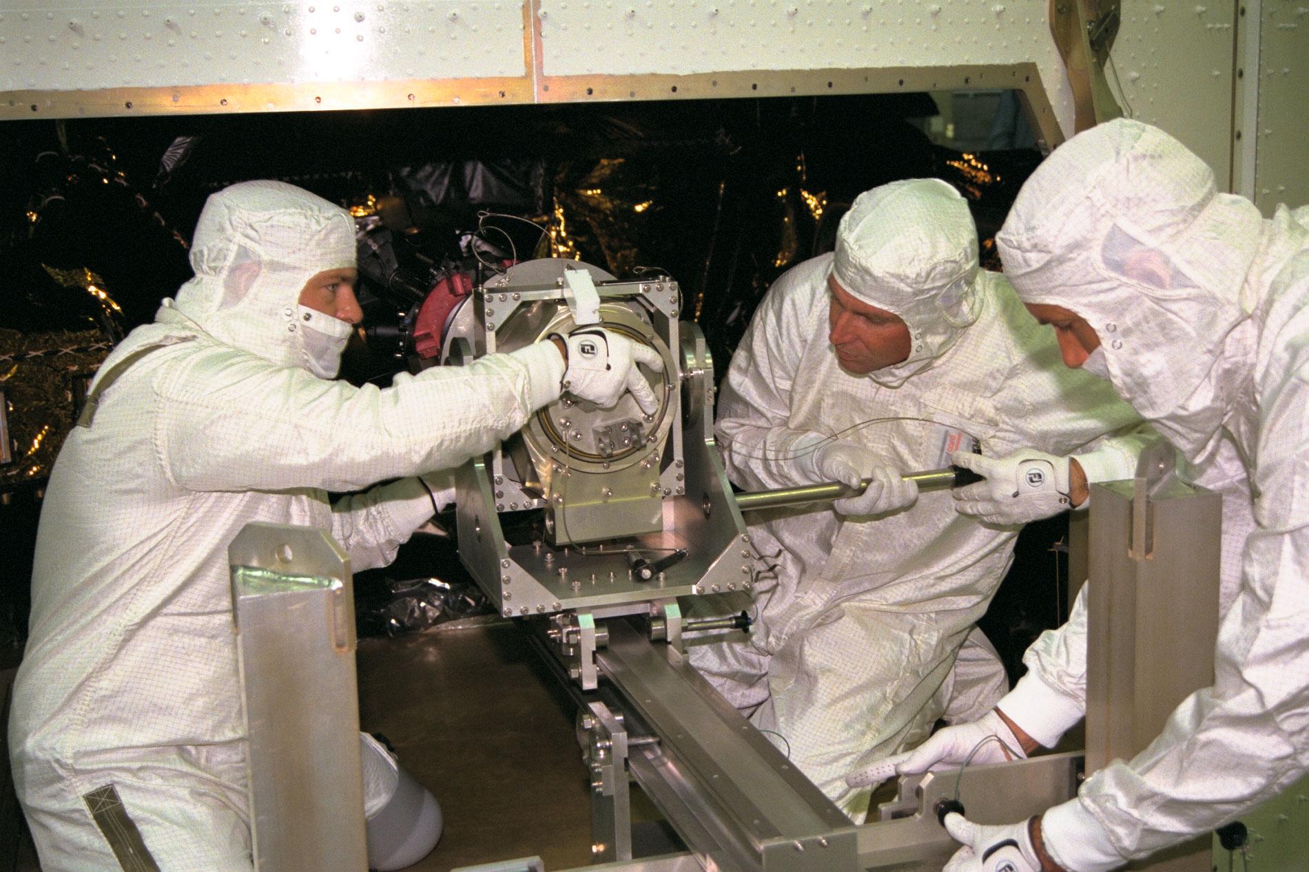 Three men install parts on a spacecraft.